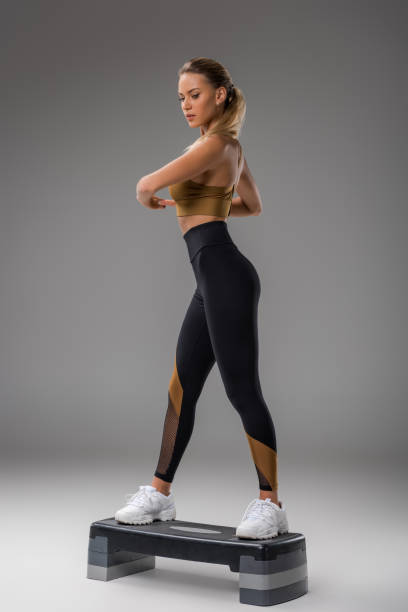 athletic young woman doing step aerobics on grey - steps imagens e fotografias de stock