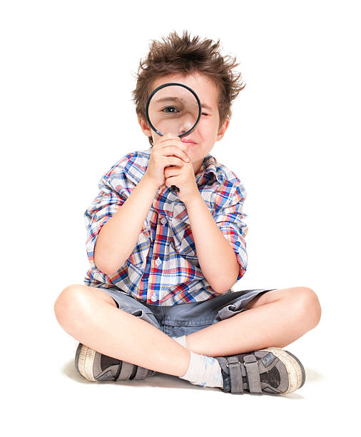 Attentive little boy with weird hair researching using magnifier stock photo