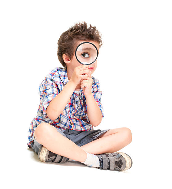 Attentive little boy with weird hair researching using magnifier stock photo