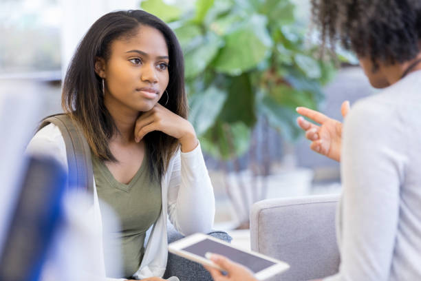 Attentive student talks with guidance counselor African American teenage girl attentively listens to a high school guidance counselor give advice. The counselor gestures while holding a digital tablet. school counselor stock pictures, royalty-free photos & images