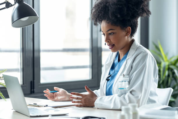 Attractive afro female doctor talking while explaining medical treatment to patient through a video call with laptop in the consultation. stock photo