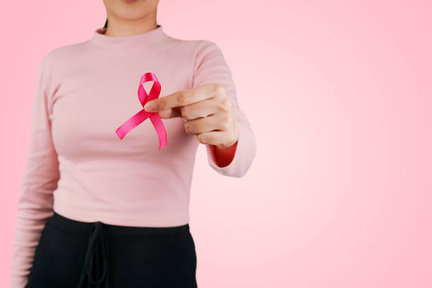 attractive asian woman or adult female holding pink ribbon symbolic of breast cancer awareness living and fighting with tumor illness.international women day and world cancer day on october concept. - world cancer day imagens e fotografias de stock