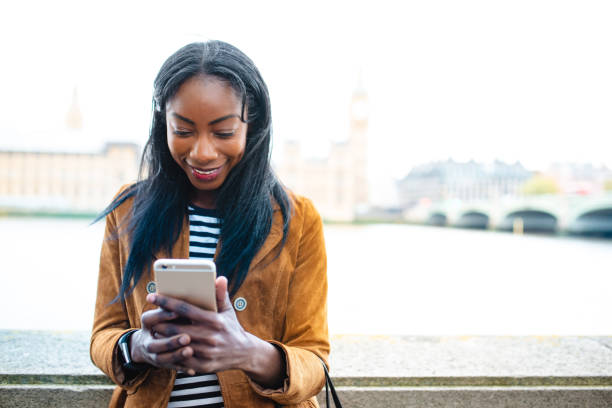 Attractive black woman smiling at her phone in front of Palace of Westminster in London stock photo