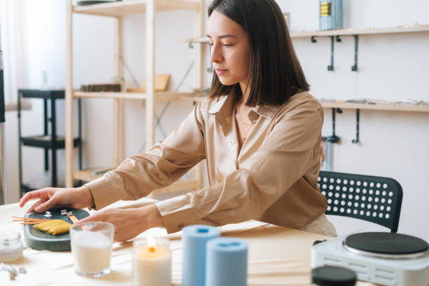 Attractive female artisan preparing workspace at table to create handmade candles in workshop. stock photo