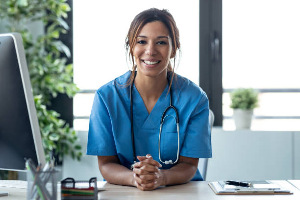 Attractive female doctor smiling looking at camera while working with laptop in the consultation. stock photo