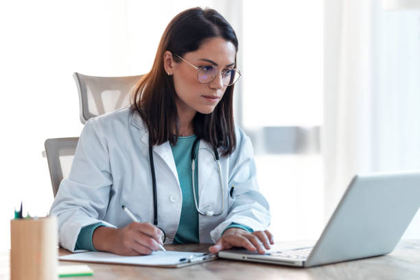 Attractive female doctor working with her computer in medical consultation. stock photo