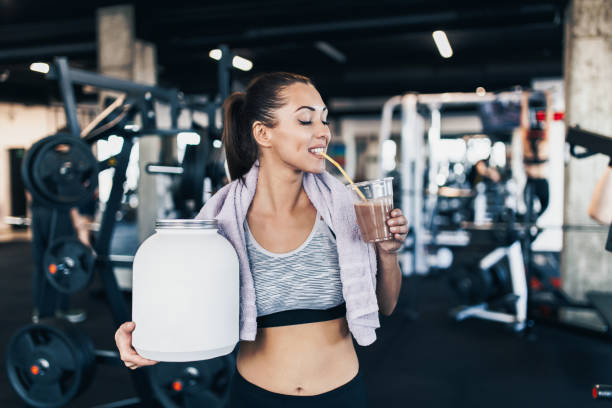atractiva mujer de ajuste que posa en gimnasio con un frasco de proteína - suplementos para entrenamiento fotografías e imágenes de stock