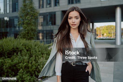 istock Attractive girl with brown hair walks out of corporate building for break, dressed in smart shirt and jacket imposed on back, walks outside past glass skyscraper, secretary, businesswoman, boss 1349414698