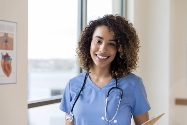 attraktive, glückliche pflegestudentin steht im krankenhausflur - krankenpflegepersonal stock-fotos und bilder