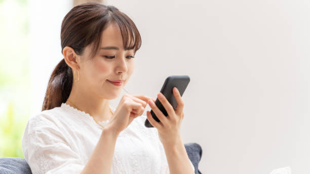 リビングルームでスマートフォンを使用して魅力的な日本の女性 - スマホ　女性　日本人 ストックフォトと画像