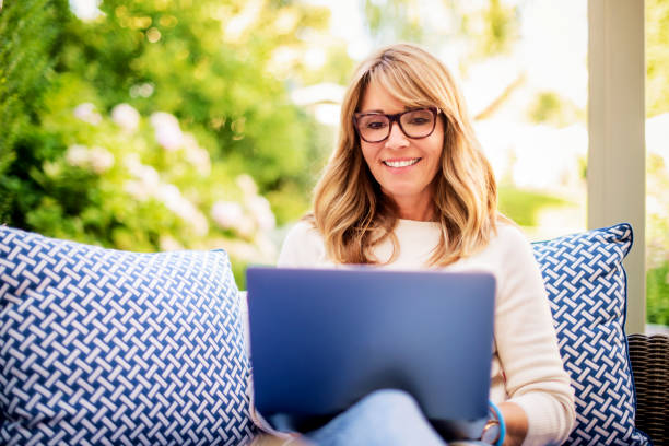 Attractive mature woman using laptop and having video call while sitting in the backyard at home stock photo