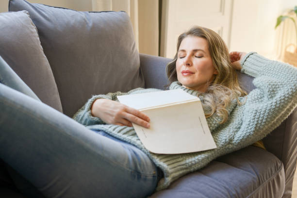 attractive middle aged woman on the couch reading a book - nap middle age woman bildbanksfoton och bilder