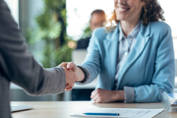 Attractive real-estate agent shaking hands with woman after signing agreement contract in a real estate stock photo