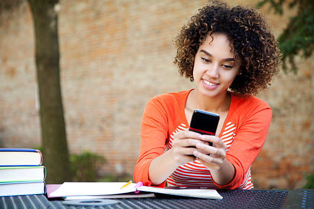 Attractive student texting Ethnic female student with curly hair wearing wearing an orange shirt and texting with her smart phone cute puerto rican girls stock pictures, royalty-free photos & images