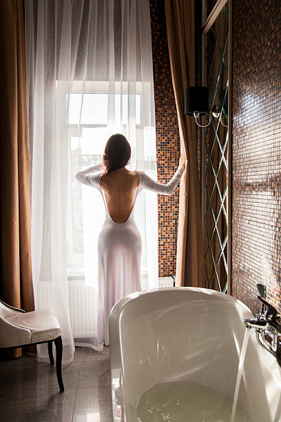 Attractive woman looking at window and preparing to take bath stock photo