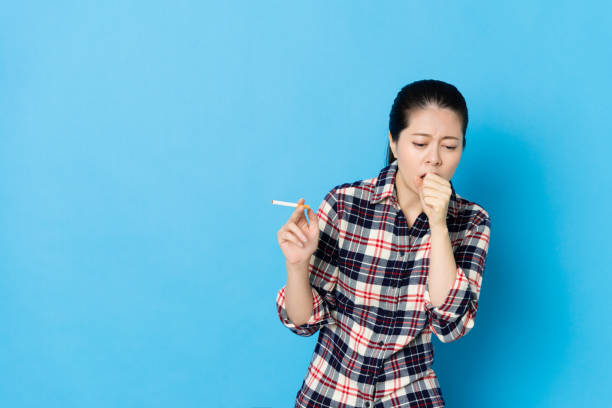 attractive young girl coughing when she smoking attractive young girl coughing when she smoking nicotine cigarette isolated on blue background. little girl smoking cigarette stock pictures, royalty-free photos & images