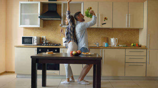 Attractive young joyful couple have fun dancing and singing while cooking in the kitchen at home stock photo