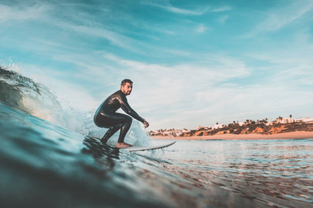 Attractive young man surfing a wave off the coast Handsome young man rides a wave off the coast with his surfboard. Extreme water sports and outdoor active lifestyle. Vintage filter with soft style surf stock pictures, royalty-free photos & images