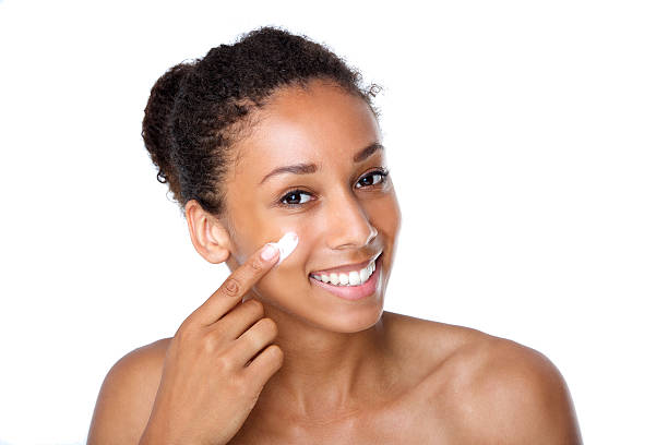 Attractive young woman applying cream on face stock photo