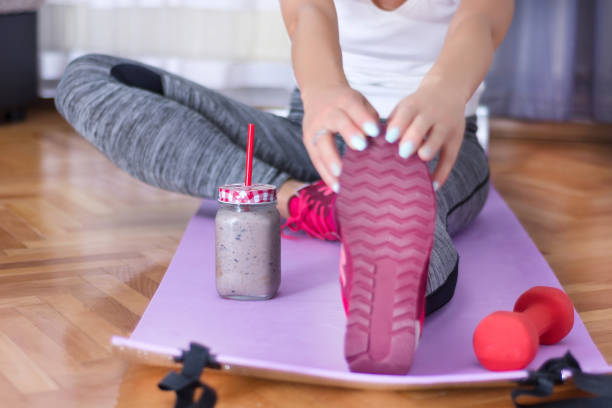 Attractive young woman muscle stretching on legs with red sneakers on purple yoga or fitness mat stock photo