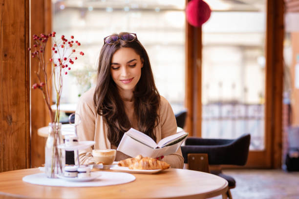 Attractive young woman sitting in the cafe and reading a book stock photo