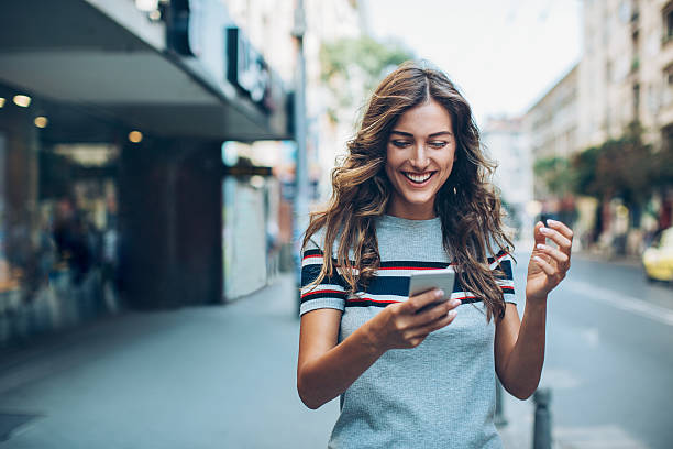 Attractive young woman texting on the street Smiling young woman with smart phone walking on the street, with copy space. teenage girls stock pictures, royalty-free photos & images