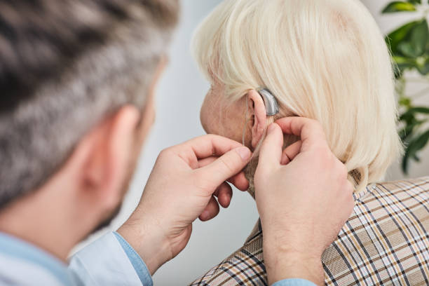 аудиолог вставляет слуховой аппарат на ухо старшей женщины крупным планом. глухота лечения, слуховое решение - hearing aids стоковые фото и изображения