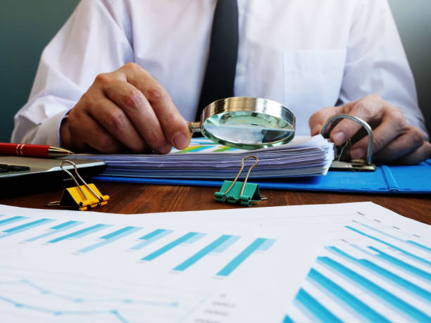 Auditor makes internal audit of company and checks financial report with magnifying glass. Auditor makes internal audit of company and checks financial report with magnifying glass. control stock pictures, royalty-free photos & images