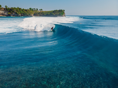 August  8, 2021. Bali, Indonesia. Aerial view with surfing on ideal barrel wave. Blue glassy waves and surfers in ocean
