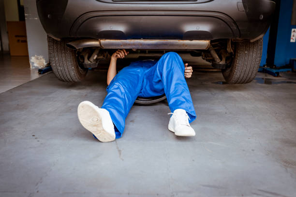 Auto mechanic working on a car engine in repair shop. Unrecognizable Person, Mechanic lying and working under car at the repair garage. Mechanic in blue uniform lying down and working under car at the auto service garage. Young mechanic lying down and working under car at the garage. Repair undercarriage service. below stock pictures, royalty-free photos & images