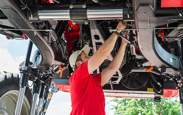 Auto mechanic working Auto mechanic working underneath a lifted agricultural machinery stock pictures, royalty-free photos & images