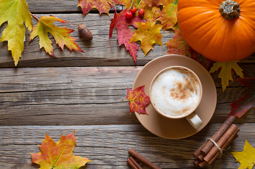 Autumn composition - cappuccino, autumn leaves and pumpkin on wooden background concept