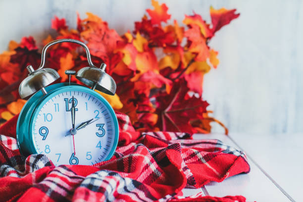 Autumn Daylight Savings Time Concept Daylight savings time concept. Set your clocks back with this retro beautiful alarm clocks set to 2 am over rustic white background with red plaid scarf and autumn leaves. Free space for text. daylight saving time stock pictures, royalty-free photos & images