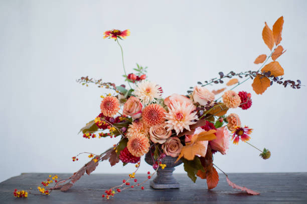 Autumn flowers bouquet in vase Beautiful flower composition with autumn orange and red flowers and berries. Autumn bouquet in vintage vase on a white wall background flower arrangement stock pictures, royalty-free photos & images