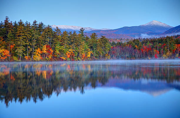 Autumn snowcapped White Mountains in New Hampshire Autumn snowcapped mountains in New Hampshire. Photo taken at dawn on a calm lake during the peak fall foliage season near the White Mountains National Forest. New Hampshire is one of New England's most popular fall foliage destinations bringing out some of  the best foliage in the United States new hampshire stock pictures, royalty-free photos & images