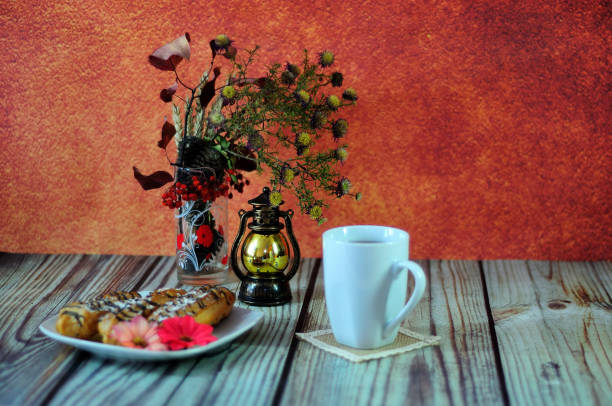 herfst stilleven, een theemok, een ouderwetse lamp, een bramen en een bord met drie eclairs staan op een tafel tegen een rode muur. - bread still life brown wall stockfoto's en -beelden