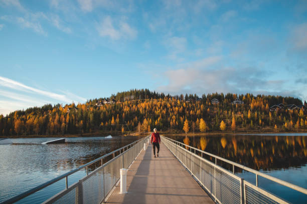 Autumn sunset at Lake Syvajarvi, in Hyrynsalmi, Finland. A young man in a plaid red and black shirt enjoys walking on a bridge at sunset. Kainuu region. Autumn in Scandinavia stock photo