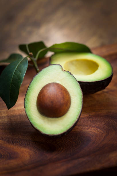 Avocado halves on wooden board with leaves stock photo