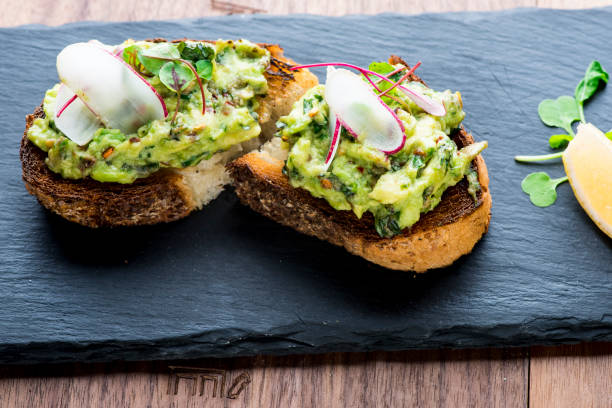 avocado Avocado toast. Classic American Diner Breakfast or Brunch Restaurant menu item. Made with fresh avocados smashed into guacamole and chopped tomatoes with salt and pepper served on wholegrain toast. toasted bread photos stock pictures, royalty-free photos & images