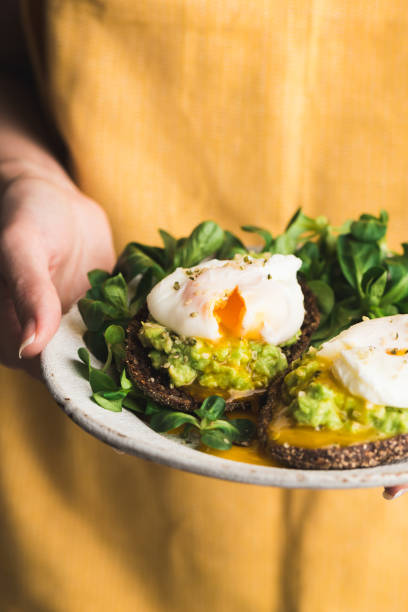 Avocado toast with poached egg Avocado toast with poached egg on plate in woman's hands. Tasty breakfast, lunch or dinner. Clean eating, healthy lifestyle concept poached food stock pictures, royalty-free photos & images
