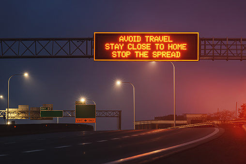 Overhead LED road sign urging people to avoid travel & stay close to home during the third wave of the COVID-19 pandemic.