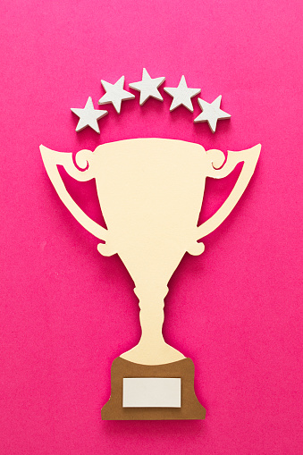 Yellow trophy made of paper on pink background with five stars over it.
