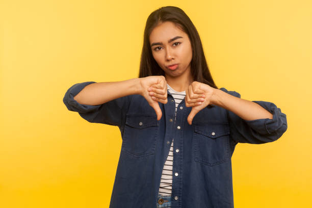 Awful result! Portrait of dissatisfied girl in denim shirt showing thumbs down, disapproval sign, gesturing dislike Awful result! Portrait of dissatisfied girl in denim shirt showing thumbs down, disapproval sign, gesturing dislike to bad service, disagree with suggestion. studio shot isolated on yellow background ugly girl stock pictures, royalty-free photos & images