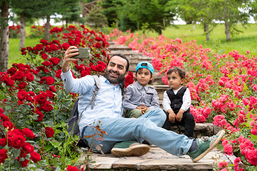 baba oğullarıyla güller arasında uzanan merdivenlerde oturmuş cep telefonu fotoğraf çekiyor. bu güzel botanik bahçesindeki aile full frame makine ile doğal ışıkta fotoğraflanmıştır.