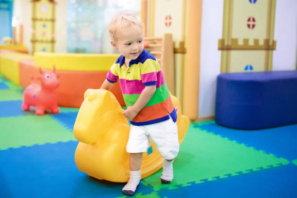 Baby boy on swing at day care play room. Kids play Child playing with hopping horse. Indoor activity toys for kids. Kindergarten or preschool play room. Toddler kid at day care playground. Swing pony for children. Baby boy with toy at daycare. indoor playground stock pictures, royalty-free photos & images