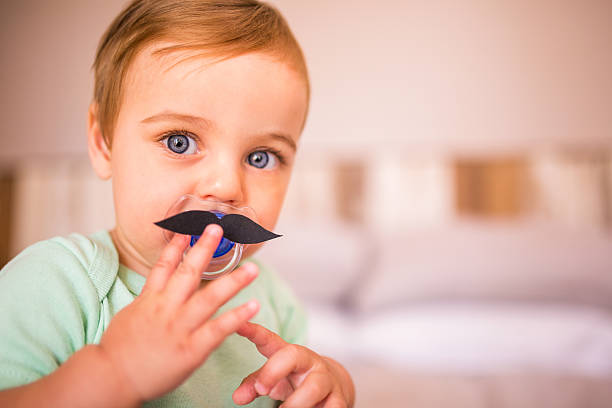 Baby boy touching a moustache that's stuck onto his pacifier stock photo