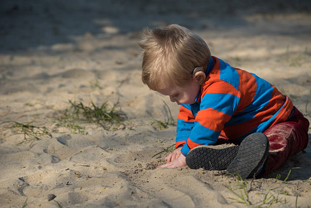 Baby boy with hearing aid digging in sand stock photo