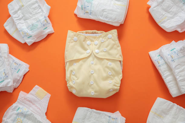Baby diaper choice concept. Yellow cloth reusable nappy and disposable diapers set on orange color background. stock photo