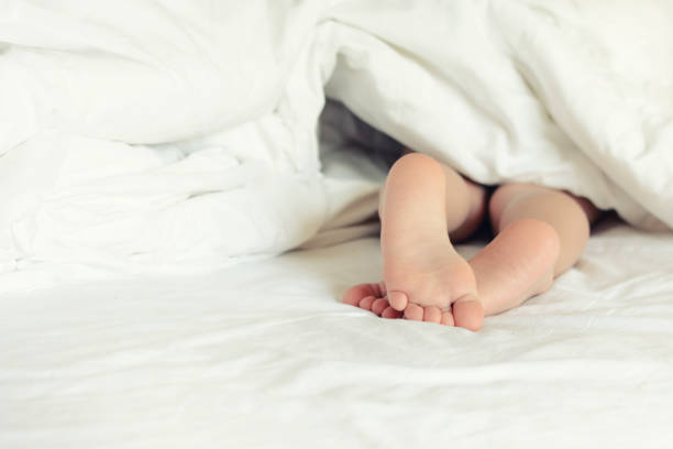 Baby feet peeking out from under the blanket. The baby lies barefoot. Bright photo with copy space. stock photo