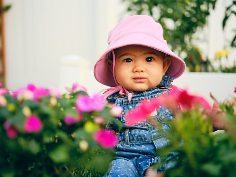 A 6 month old baby girl wearing overalls in a backyard garden.